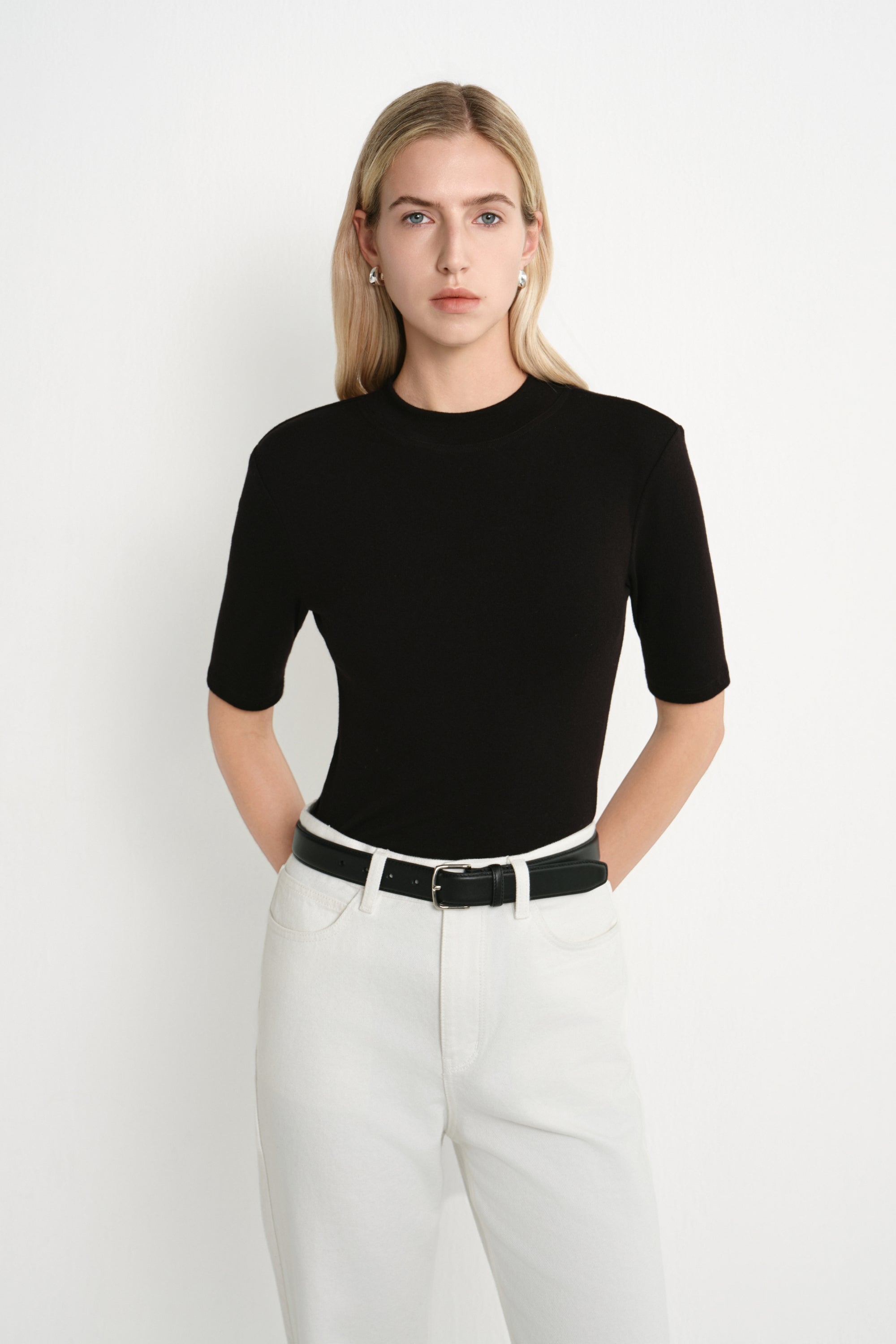 A model wearing the Rue Sophie Chabot Mock Neck Top in black, highlighting the fitted silhouette, structured shoulders, and clean mock neckline, front view.