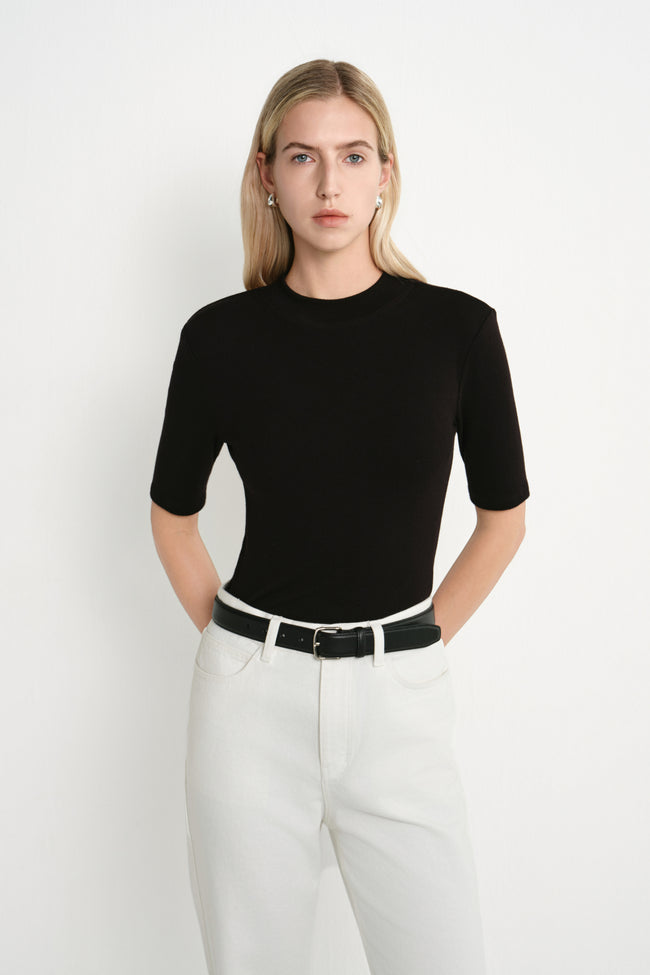 A model wearing the Rue Sophie Chabot Mock Neck Top in black, highlighting the fitted silhouette, structured shoulders, and clean mock neckline, front view.