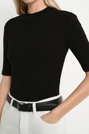 A model wearing the Rue Sophie Chabot Mock Neck Top in black, featuring a fitted silhouette, mock neckline, and elbow-length sleeves, front view.