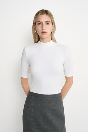 A model wearing the Rue Sophie Chabot Mock Neck Top in cream, featuring a fitted silhouette, clean mock neckline, and elbow-length sleeves, three-quarter front view.