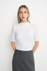 A model wearing the Rue Sophie Chabot Mock Neck Top in cream, featuring a fitted silhouette, clean mock neckline, and elbow-length sleeves, three-quarter front view.