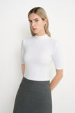A model wearing the Rue Sophie Chabot Mock Neck Top in cream with a fitted silhouette, mock neckline, and elbow-length sleeves, front view.