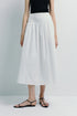 White cotton A-line skirt with pintuck detailing, styled with black top and sandals.
