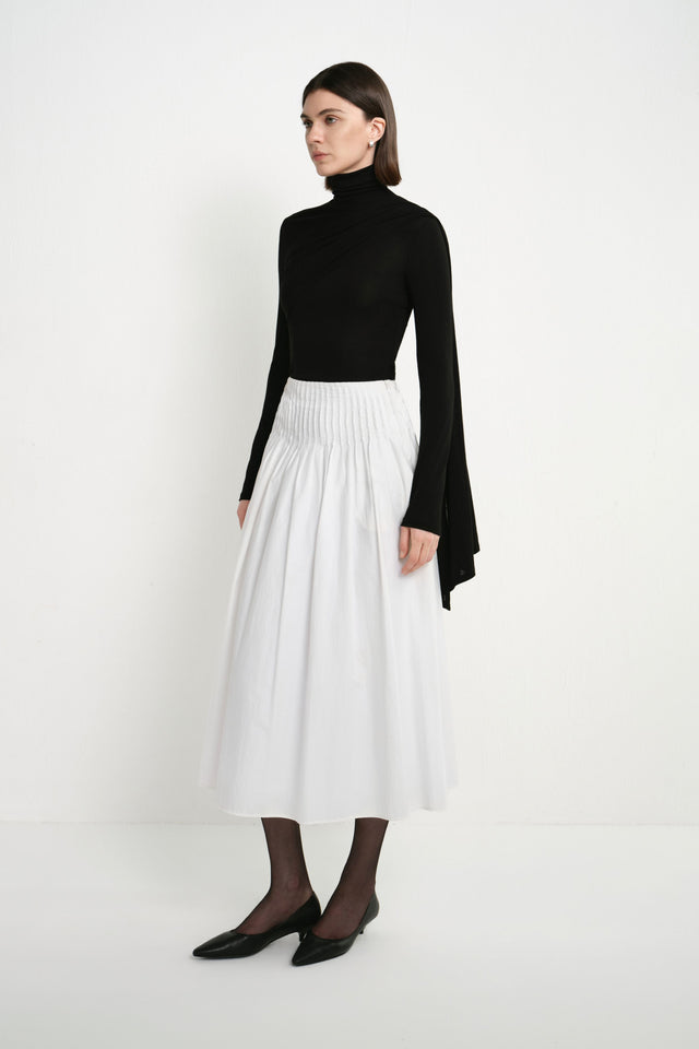 A model wearing the Rue Sophie Piquenique Pintuck Skirt in white, highlighting the high pintucked waistband, gathered volume, side pockets, and flowing midi length, three-quarter view.