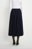 Back view of a model wearing the Rue Sophie Panier Drawstring Waist Pleated Skirt in Navy, showing the elasticated waist and full gathered silhouette.