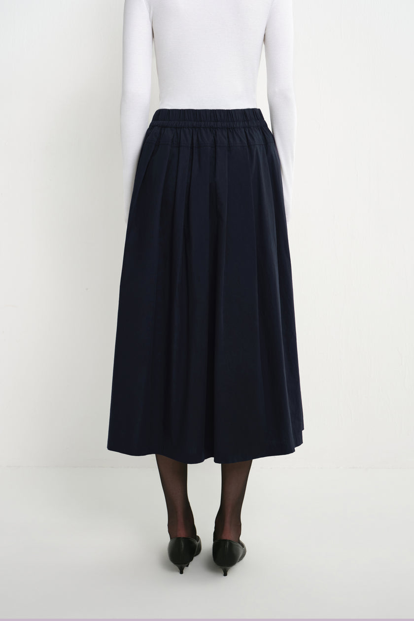 Back view of a model wearing the Rue Sophie Panier Drawstring Waist Pleated Skirt in Navy, showing the elasticated waist and full gathered silhouette.