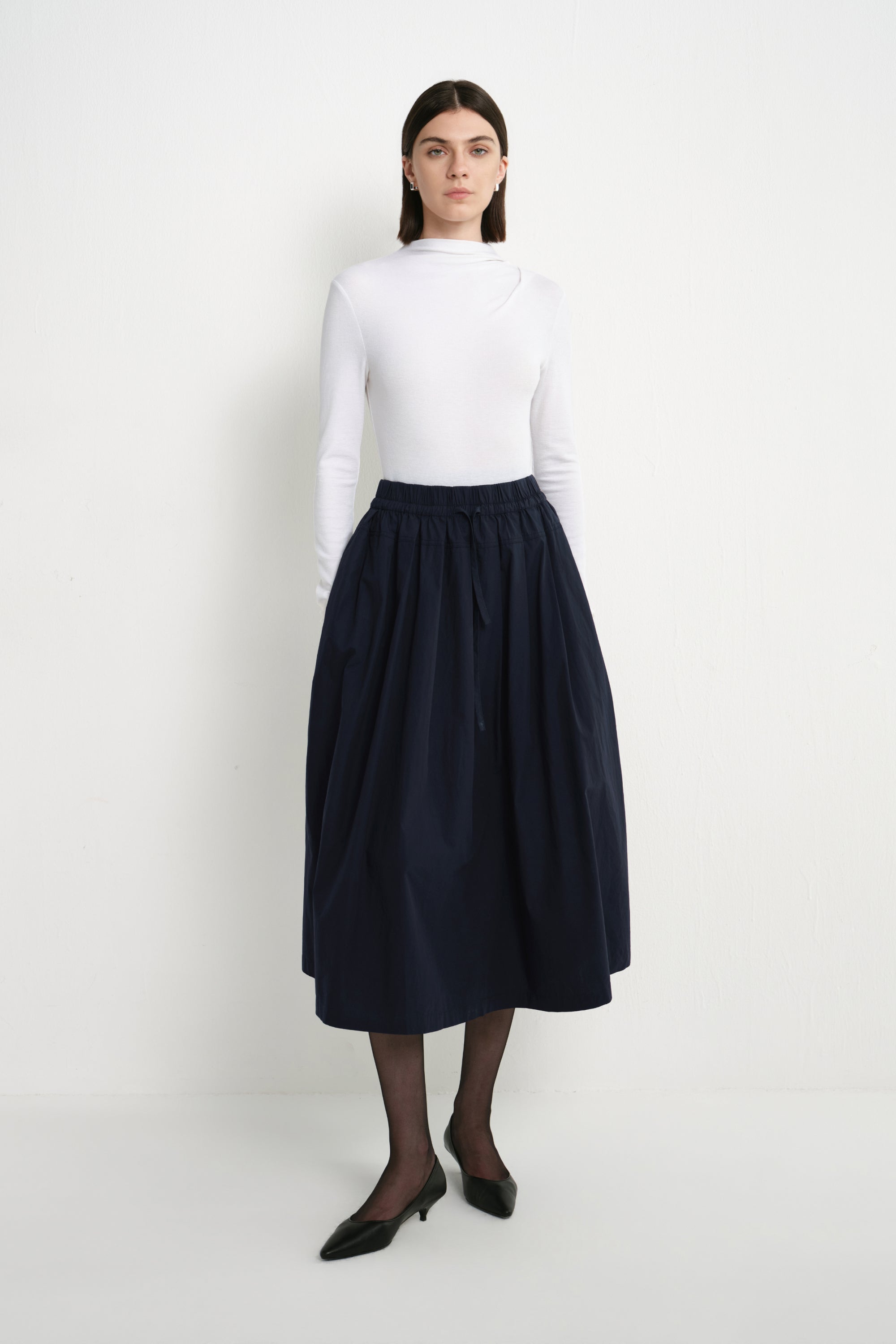 Front view of a model wearing the Rue Sophie Panier Drawstring Waist Pleated Skirt in Navy, highlighting the drawstring waist and full midi silhouette.