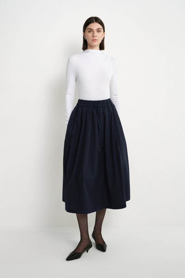 Front view of a model wearing the Rue Sophie Panier Drawstring Waist Pleated Skirt in Navy, highlighting the drawstring waist and full midi silhouette.
