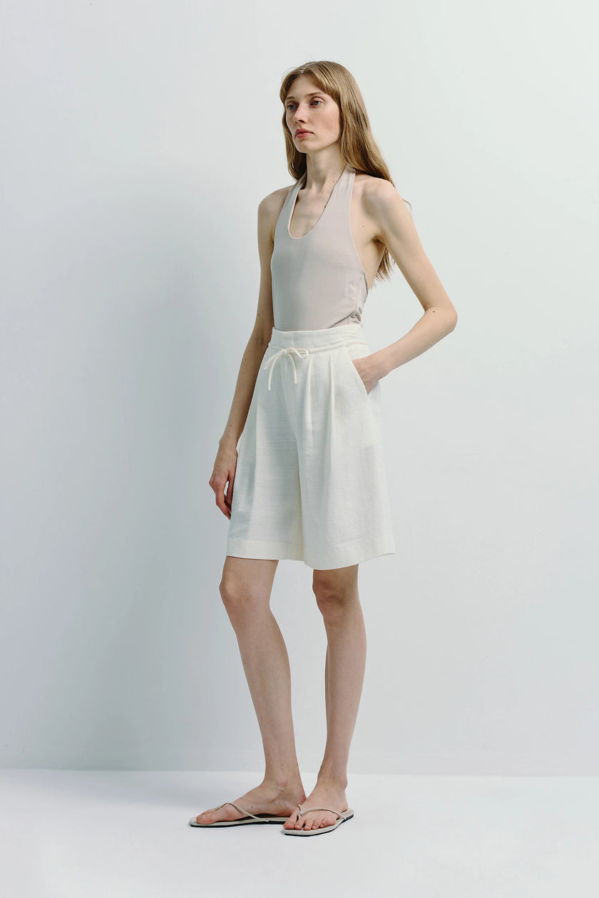 White linen blend Arc Tie Waist Short with adjustable tie waist, styled with a halter top.