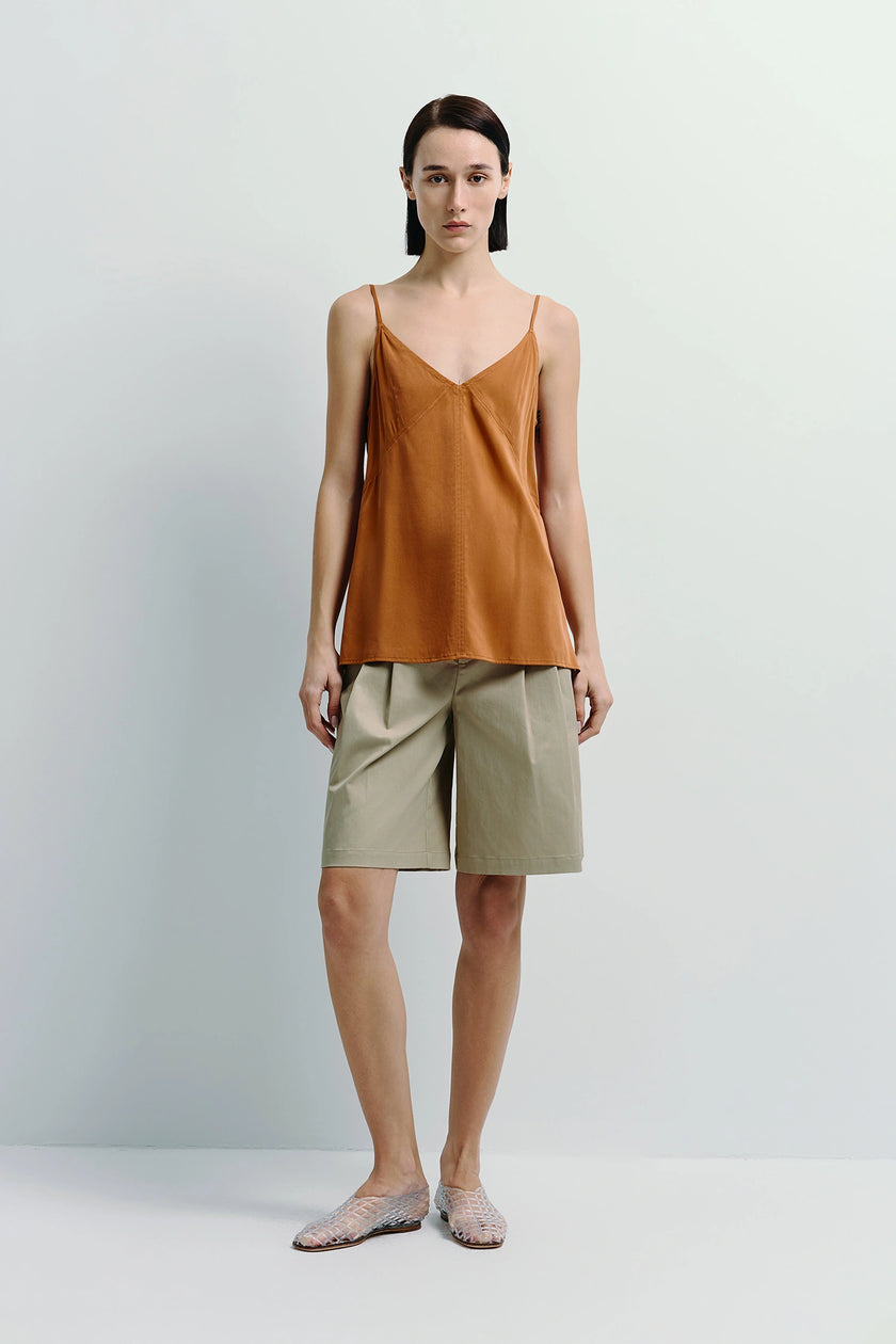 Woman in burnt orange camisole and pleated beige Bermuda shorts.