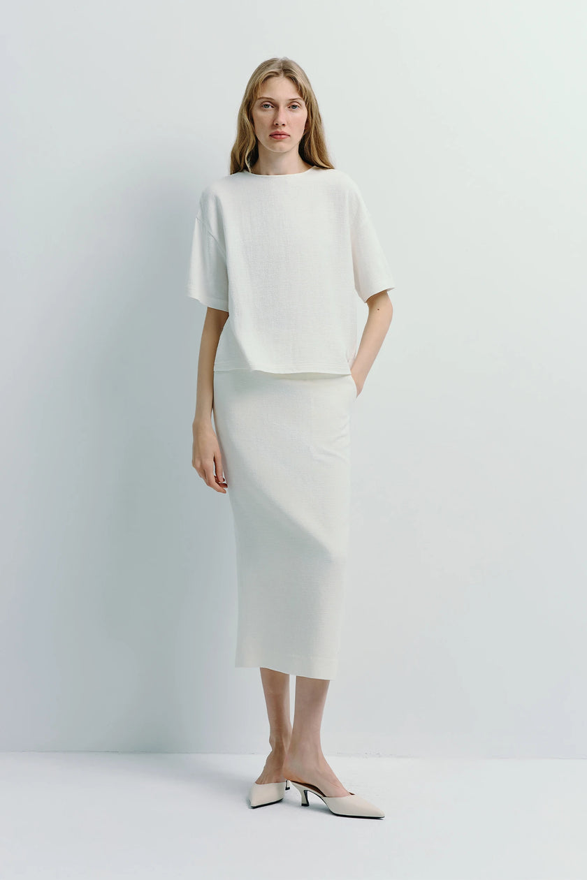 Woman wearing a structured white linen blend pencil skirt and top, minimalist, timeless style.