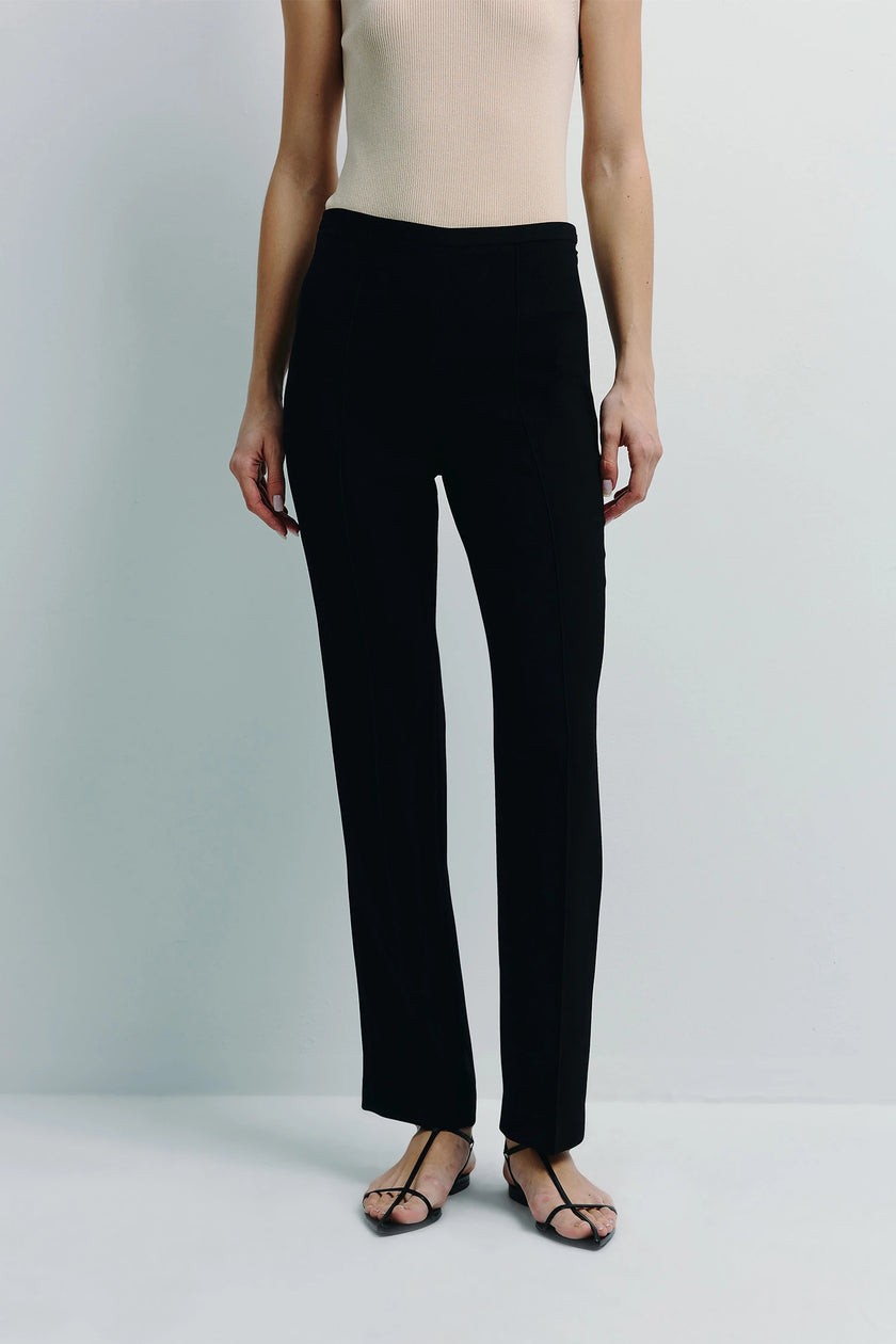 Black Coupe Tapered Leg Slim Pant, showcasing a tailored fit and slim leg, paired with a cream top and minimalist sandals