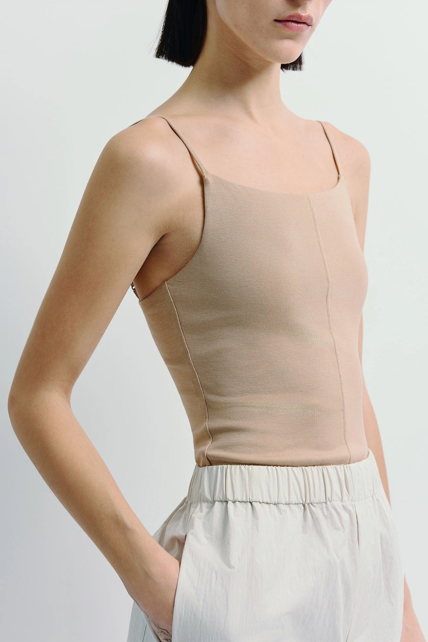 Aride Cami Bodysuit in beige, showcasing the soft viscose blend, paired with light trousers. Minimal and versatile.