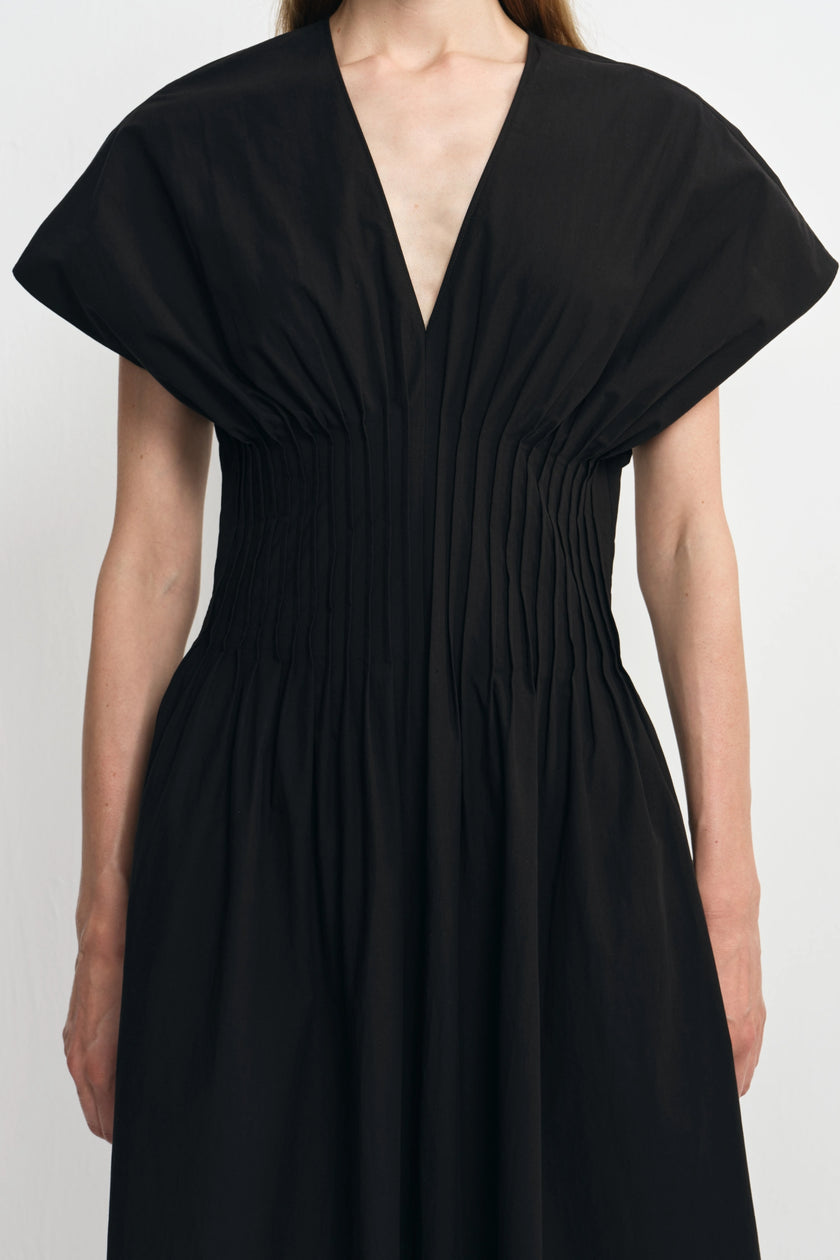 A black midi dress with a deep V-neckline, gathered pleated bodice, and wide short sleeves, shown on a model against a light gray background.