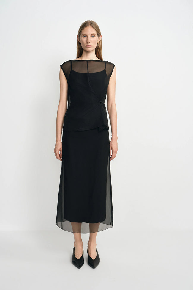 Woman wearing a black dress with sheer overlay on a white background