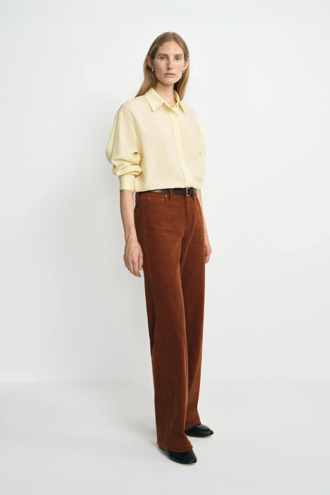 A model wearing the Rue Sophie Naya Button Down Shirt in Italian Straw with brown corduroy trousers, shown in a three-quarter view with rolled sleeves.