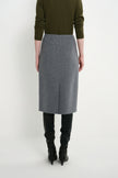 A model shown from the back wearing a gray wool-blend midi skirt, an olive green sweater, and black knee-high boots against a plain white studio background.