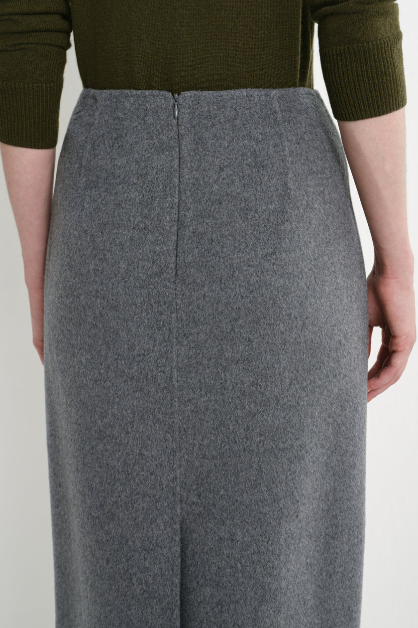 A close-up of a person wearing a high-waisted, knee-length gray wool skirt with a front zipper, paired with an olive green ribbed knit top.