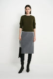 A model stands against a plain light gray studio background wearing a color-blocked sweater and skirt set. The top is olive green, the middle band is white, and the skirt is heather gray.