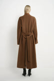A model viewed from the back wearing a long brown belted coat and black ankle boots against a plain white studio background.