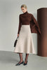 A model wearing a dark brown draped turtleneck top with an extended asymmetric shoulder panel, styled with a light beige A-line midi skirt and black pointed pumps.