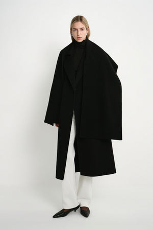 A model wearing the Rue Sophie Grand Scarf Coat in black with an oversized scarf draped over the shoulders, long sleeves, and a relaxed midi silhouette, full-length front view.