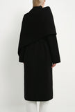 Back view of a model wearing the Rue Sophie Grand Scarf Coat in black, featuring an oversized scarf panel, belted waist, and clean long-line silhouette.