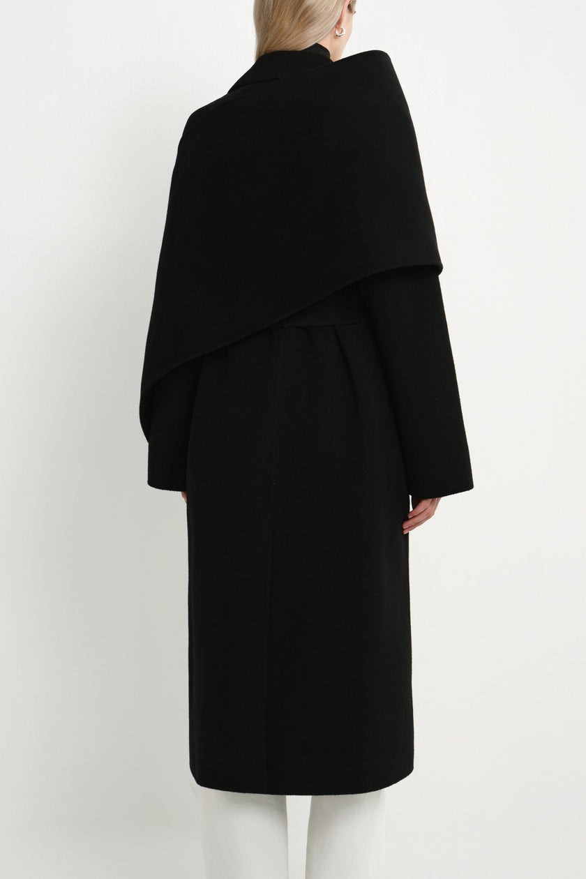 Back view of a model wearing the Rue Sophie Grand Scarf Coat in black, featuring an oversized scarf panel, belted waist, and clean long-line silhouette.