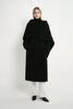A model wearing the Rue Sophie Grand Scarf Coat in black, featuring an oversized draped scarf panel, belted waist, long sleeves, and a clean midi silhouette, front view.