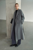 A model wearing the Rue Sophie Martine Belted Coat in grey, featuring wide notched lapels, side pockets, and a relaxed ankle-length silhouette, three-quarter front view.