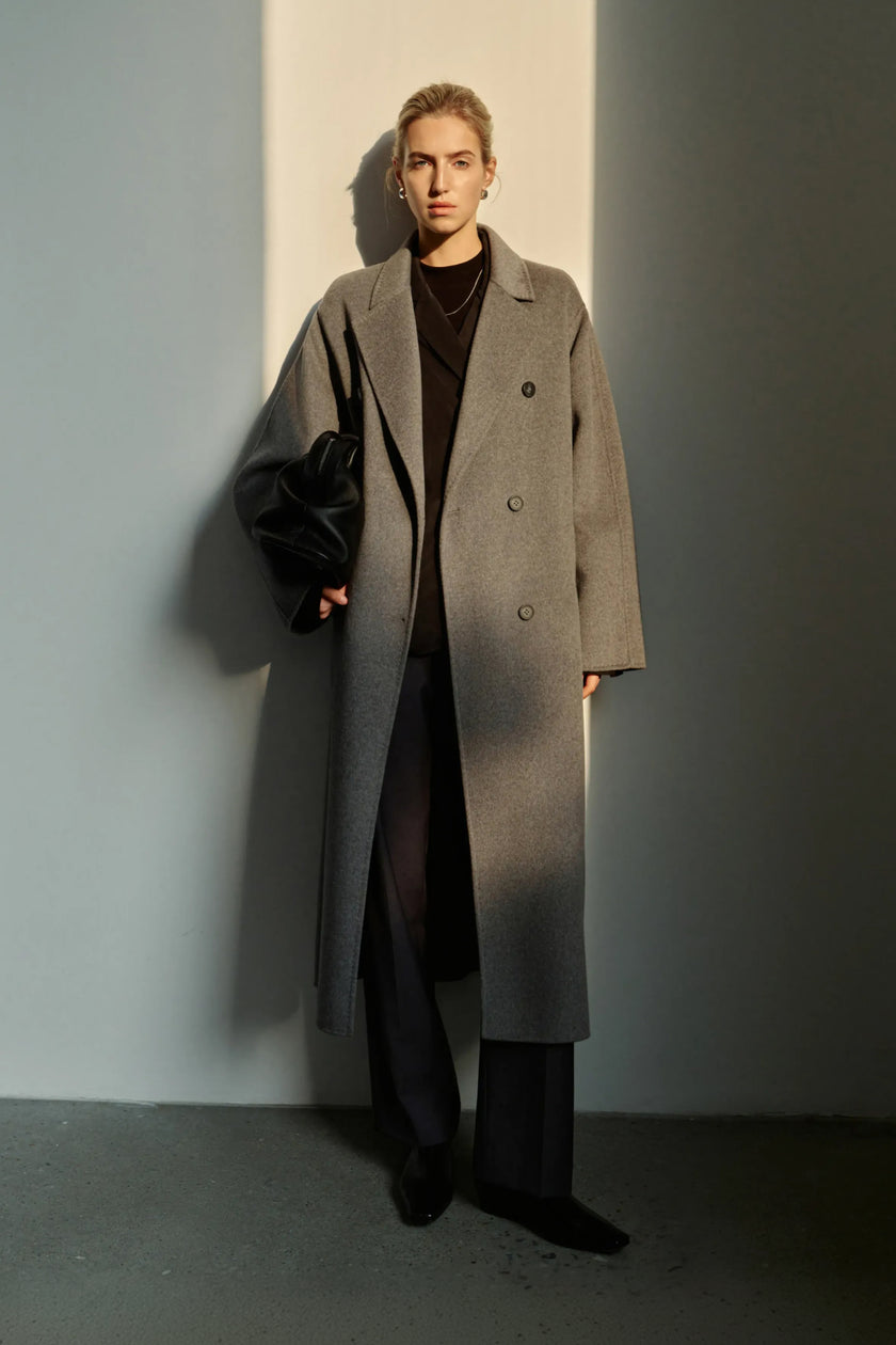 A model wearing the Rue Sophie Martine Belted Coat in grey, featuring wide notched lapels, a button-front design, and a relaxed longline silhouette, front view.