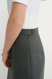 Close-up side view of a person wearing a dark gray textured skirt with a single button closure at the waistband, paired with a white top against a plain light background.