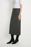A model wearing a dark gray, mid-calf length skirt with rolled cuffs, styled with a white top and black pointed-toe ankle boots against a plain white studio background.