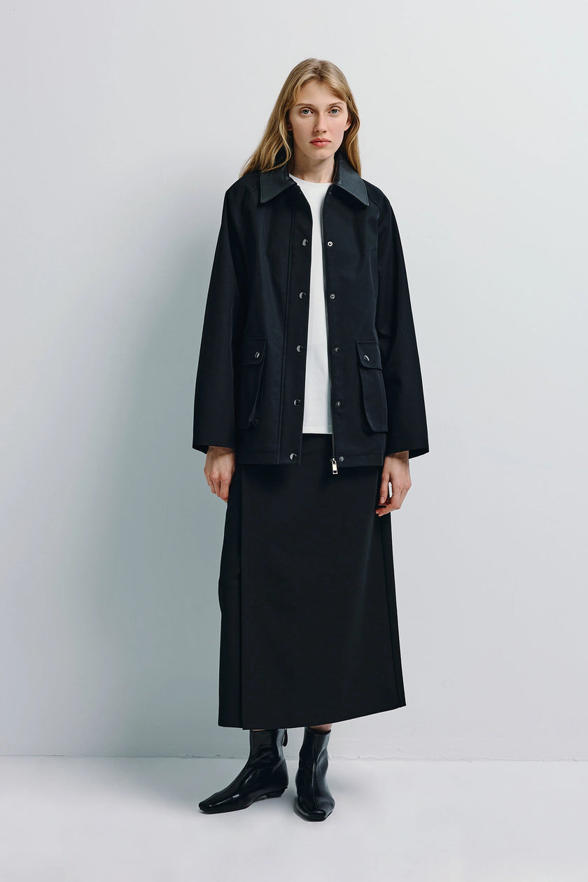 Black midi skirt with side slit paired with a black jacket and boots, a modern ensemble.