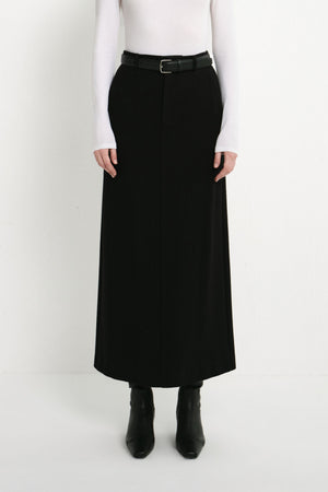 A model wearing the Rue Sophie Camberly Midi Skirt in black with a high waist, belt loops, center-front seam, and long structured silhouette, front view.