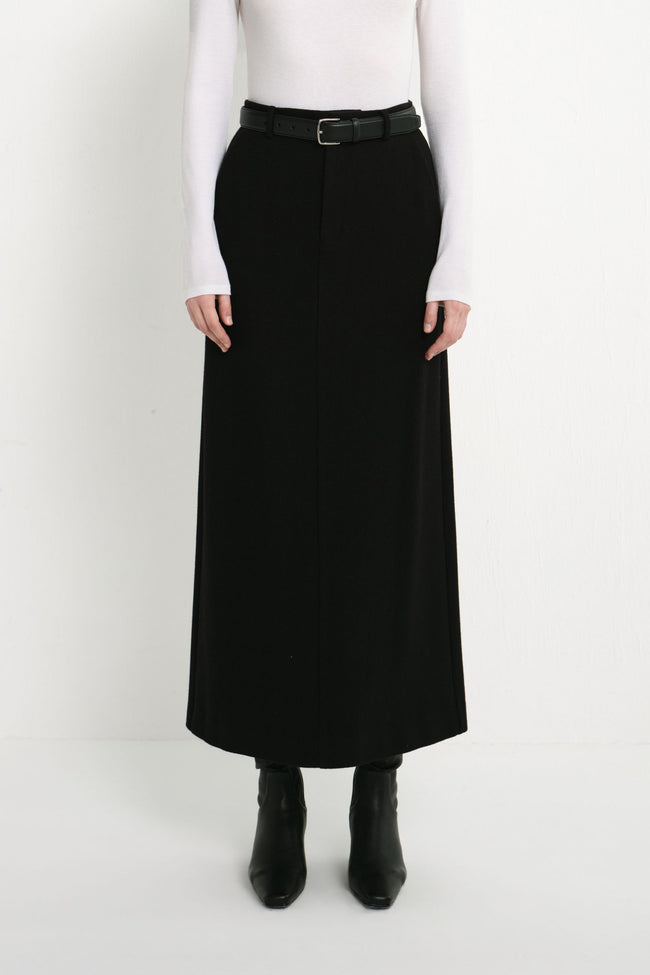 A model wearing the Rue Sophie Camberly Midi Skirt in black with a high waist, belt loops, center-front seam, and long structured silhouette, front view.