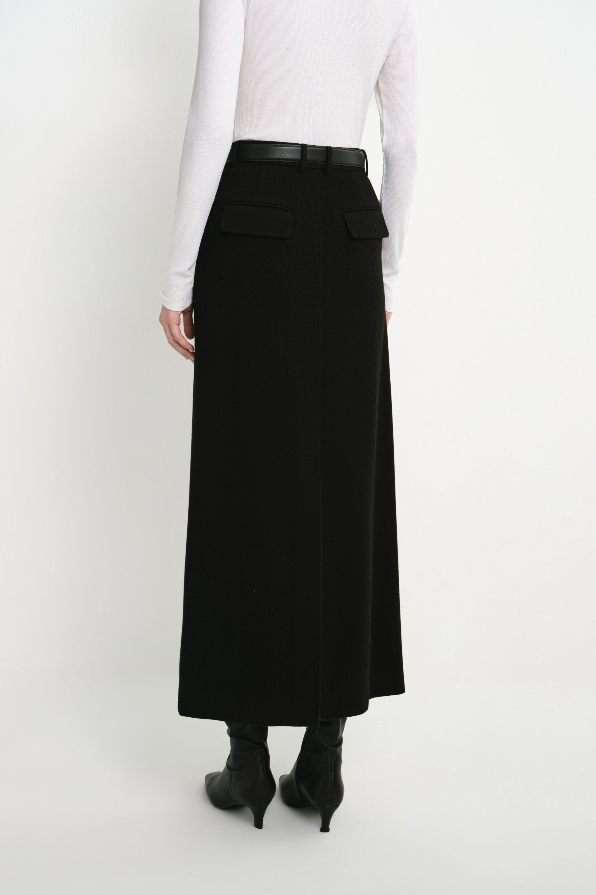 Back view of a model wearing the Rue Sophie Camberly Midi Skirt in black, featuring a high waist, belt loops, flap back pockets, and center-back seam.
