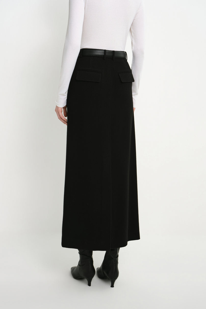 Back view of a model wearing the Rue Sophie Camberly Midi Skirt in black, featuring a high waist, belt loops, flap back pockets, and center-back seam.