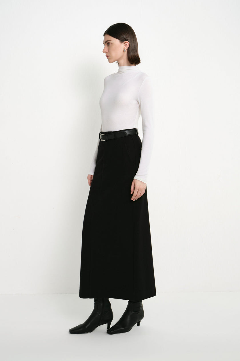Side view of a model wearing the Rue Sophie Camberly Midi Skirt in black, featuring a high-waisted fit and clean elongated A-line silhouette.