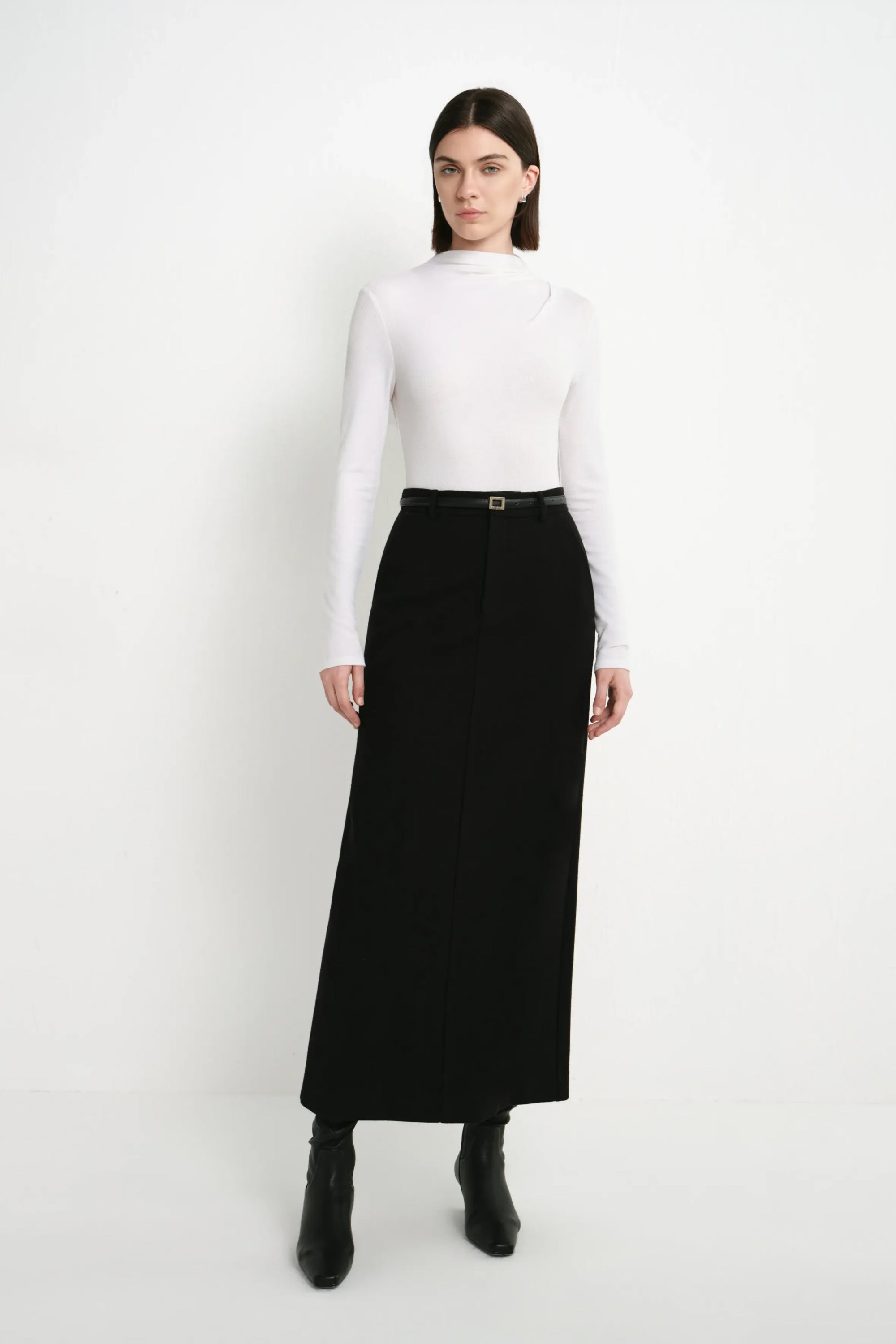 A model wearing the Rue Sophie Camberly Midi Skirt in black with a high waist, clean center-front construction, and streamlined long silhouette, front view.