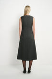 A woman viewed from the back wearing a sleeveless dark gray A-line midi dress, black tights, and black heels against a plain white studio background.