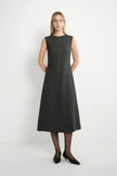 A woman modeling a sleeveless, knee-length dark gray A-line dress with a textured weave, paired with black tights and black pointed-toe heels, against a plain white studio background.