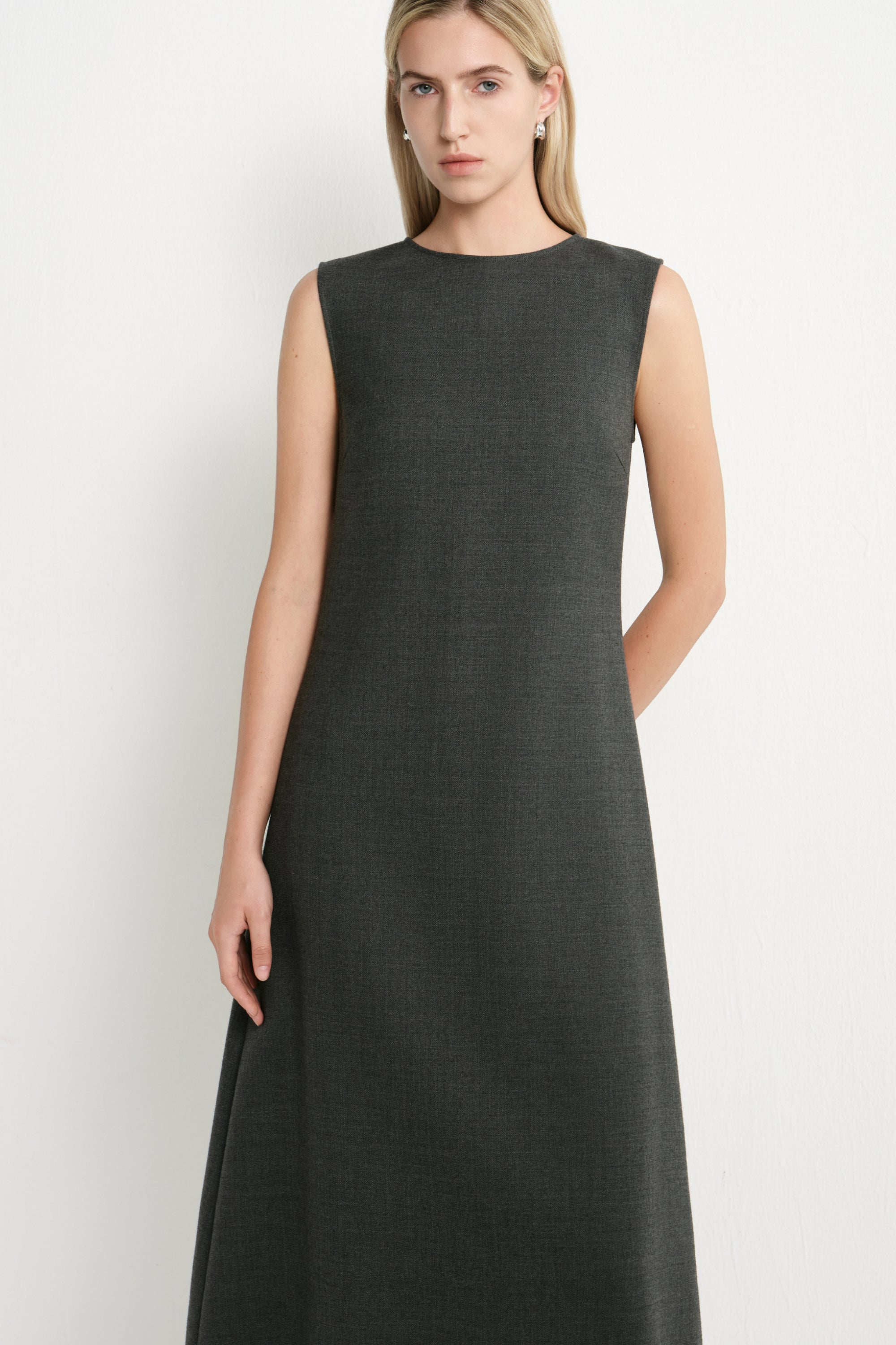 A woman modeling a sleeveless, dark charcoal gray midi dress against a plain light gray studio background.