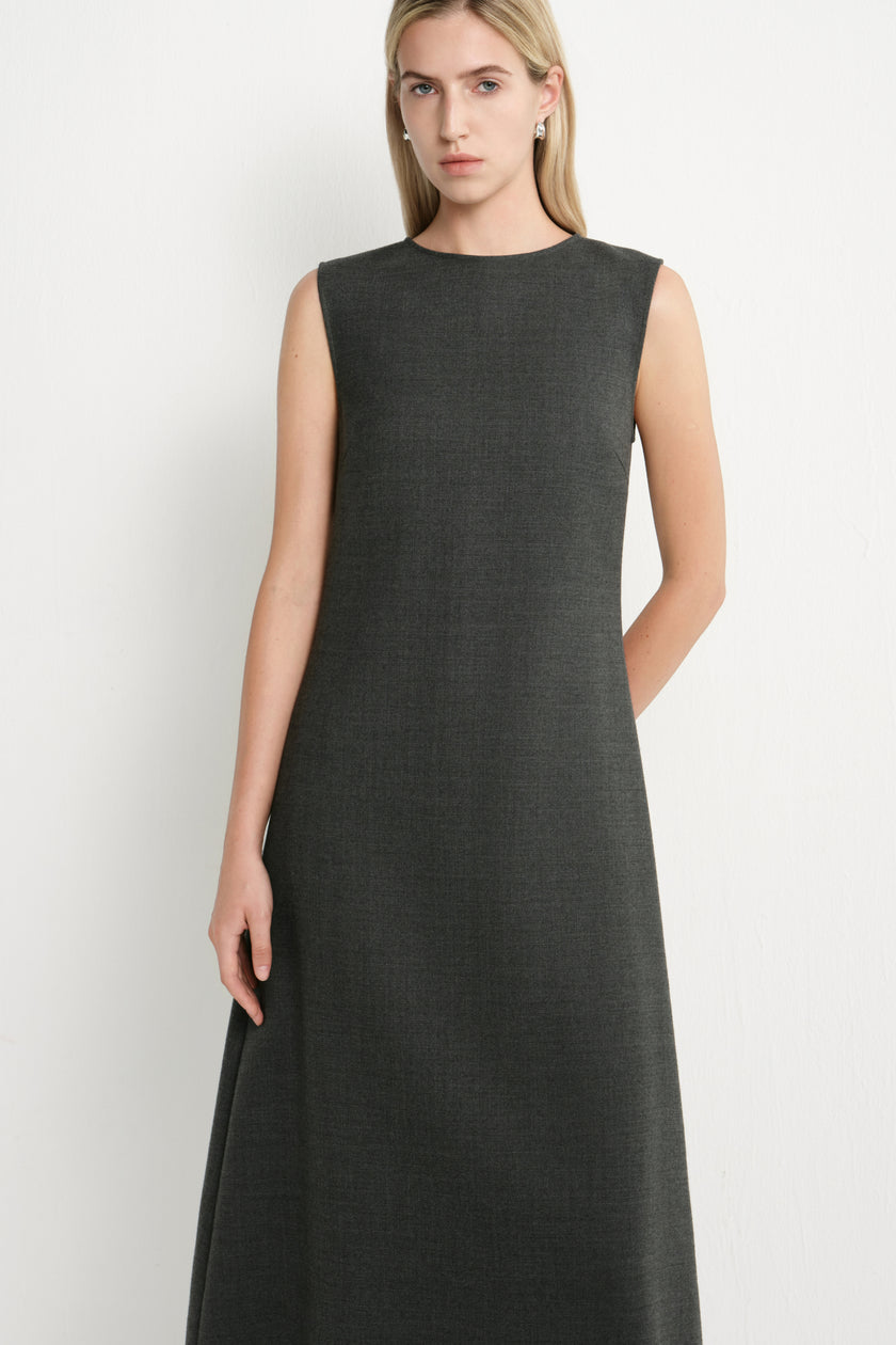 A woman modeling a sleeveless, dark charcoal gray midi dress against a plain light gray studio background.