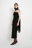 A model wearing the Rue Sophie Webster Tube Dress in black with a straight strapless neckline and fitted mid-calf silhouette, styled with a draped black scarf, three-quarter side view.