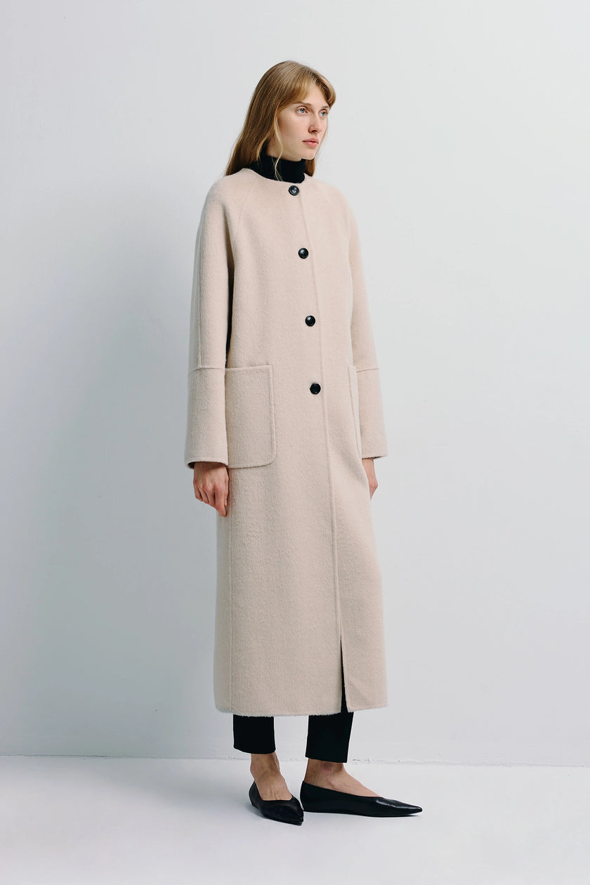 Iana Collarless Handmade Coat in light beige wool-alpaca blend, featuring black buttons and kangaroo pockets.