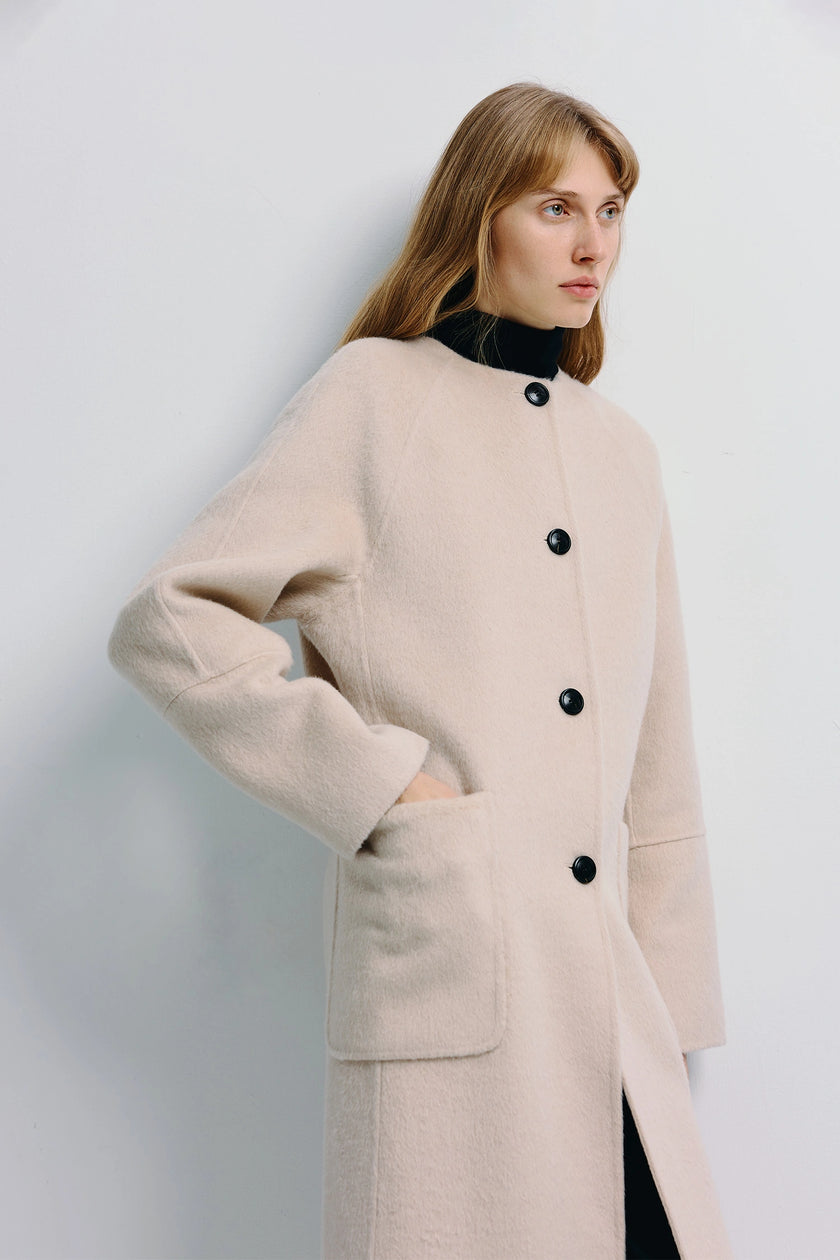 Iana Collarless Handmade Coat in light beige, featuring black buttons and kangaroo pockets