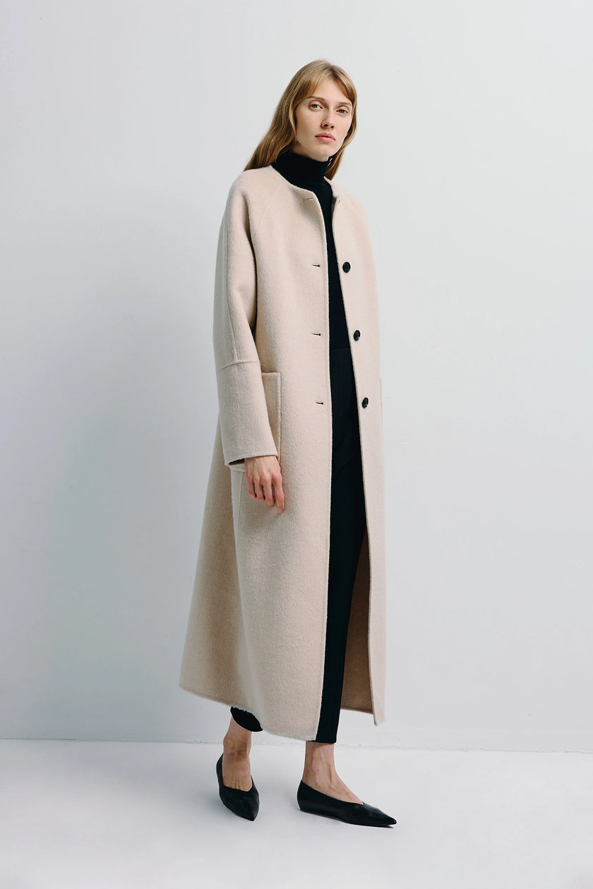 Iana Collarless Handmade Coat in light beige, woman in black turtleneck and pants