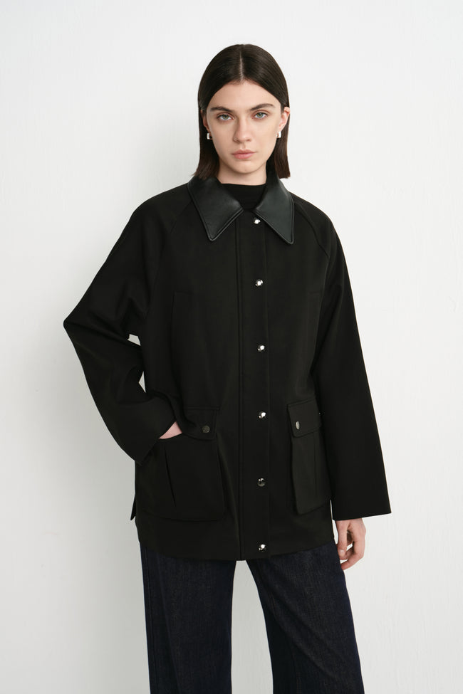A model wearing the Rue Sophie Roth Leather Barn Jacket in black with a contrast leather collar, metallic snap buttons, flap patch pockets, and a relaxed straight fit, front view.