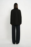 A model shown from the back wearing a black long-sleeve blazer and dark wide-leg trousers against a plain white studio background.